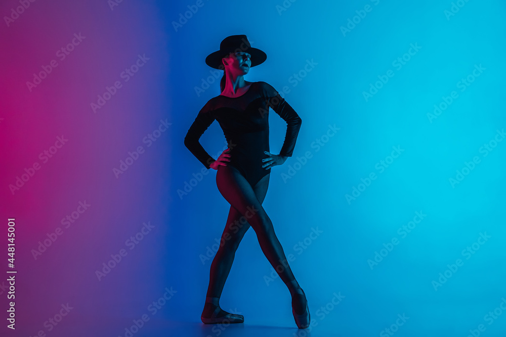 Contemporary ballet dancer woman in hat posing on multi-colored gradient pink blue background. Professional ballerina in sexy costume of femme fatale, solo performance.
