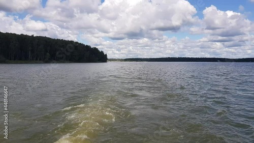 Motor boat trip along the waves of the picturesque Senezh lake. Skyline, green trees on the shore and cloudy blue sky on a sunny day. Moscow region, Russia