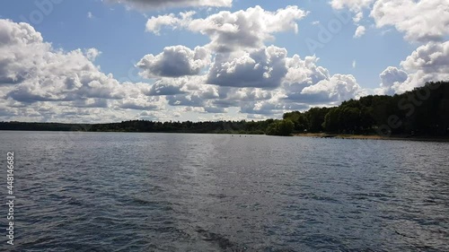 Motor boat trip along the waves of the picturesque Senezh lake. Skyline, green trees on the shore and cloudy blue sky on a sunny day. Moscow region, Russia