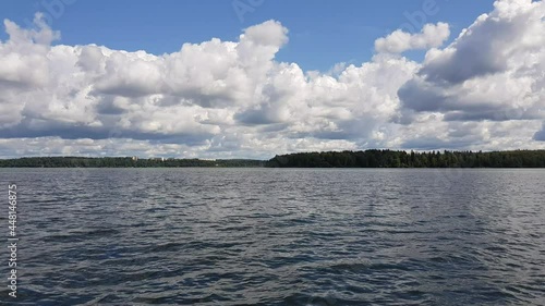 Motor boat trip along the waves of the picturesque Senezh lake. Skyline, green trees on the shore and cloudy blue sky on a sunny day. Moscow region, Russia