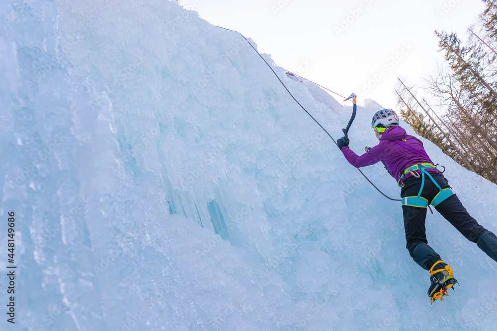 Female ice climber silhouette swinging ice axes on her way up vertical ice waterfall, side view