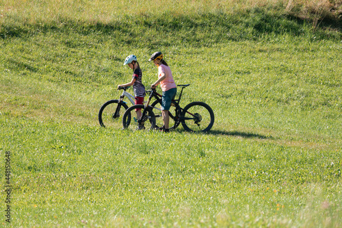 Two females on mountain bikes talking and looking at beautiful green nature.