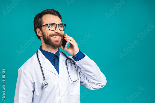 Close up shot of handsome young man doctor isolated on blue background talking on smartphone, smiling positively. Using mobile phone.