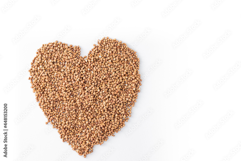 Raw buckwheat groats on a white background in the shape of a heart.Close-up of buckwheat porridge. Valentine's Day background.
