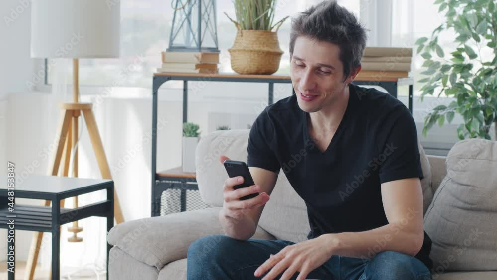 Caucasian millennial man blogger sitting at home couch on lockdown quarantine speaks into cell phone camera makes online video call conference remotely smartphone kisses screen waves hello goodbye Caucasian millennial man blogger sitting at home couch on lockdown quarantine speaks into cell phone camera makes online video call conference remotely smartphone kisses screen waves hello goodbye