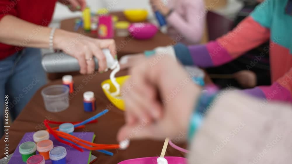 Hand of woman teacher squeezing shaving foam into bowls standing in