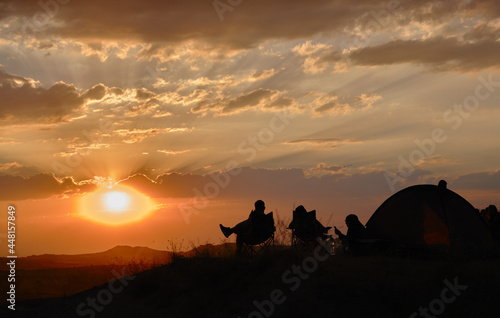 Sunset watching in rose valley sunset (kizil vadi) with silhouette of tourists and people sitting in picnic chairs and near camping tent