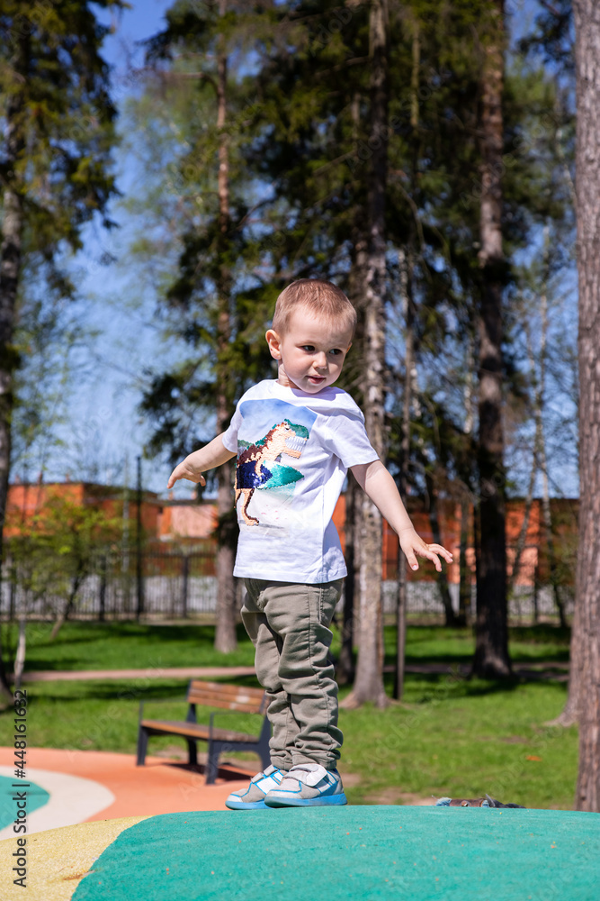 Fototapeta premium little boy walks through the territory of the playground outdoors on sunny day.