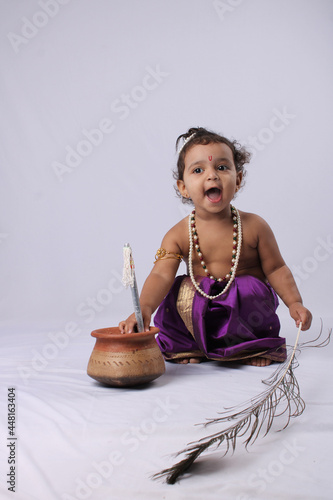 adorable Indian baby in krishna kanha or kanhaiya dress posing with his flute and peacock feather on white background. standing pose photo