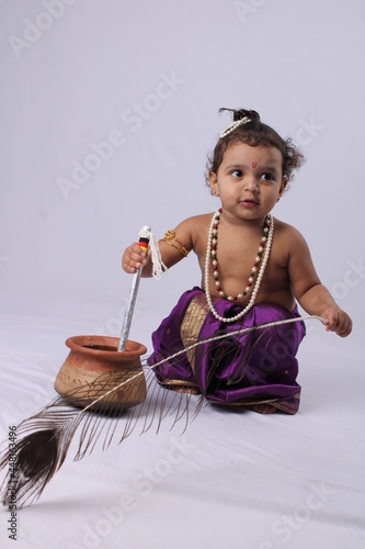 adorable Indian baby in krishna kanha or kanhaiya dress posing with his flute and peacock feather on white background. standing pose photo