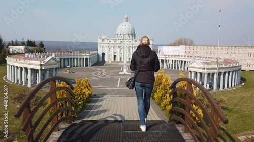 A steady shot of Woman makes photo walking on foot near a miniature model of the Saint Peter's Basilica, Vatican. Park of Miniatures. Kielce, Poland - April 1, 2019.