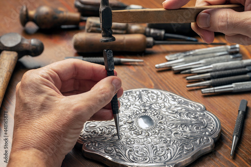 CRAFTSMAN'S HAND EMBOSSING METAL WITH PUNCH AND HAMMER IN THE WORKSHOP. SILVERSMITH, JEWELLERY AND HANDICRAFTS CONCEPT. photo