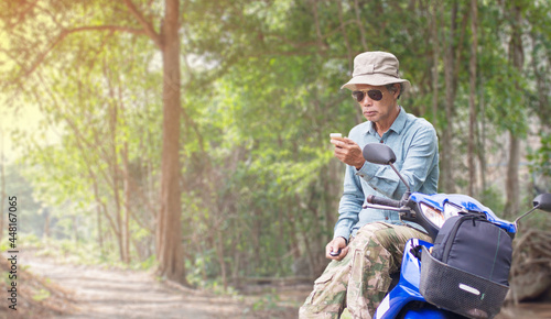 Senior man traveling on a motorcycle in the forest using a smartphone