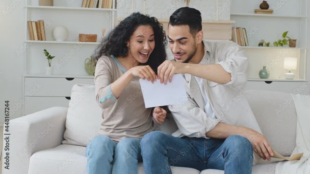 Spaniard hispanic married couple ethnic family sit on sofa at home receive letter document by mail notice from bank with good news read paper win lottery money rejoice celebrate shout with happiness Spaniard hispanic married couple ethnic family sit on sofa at home receive letter document by mail notice from bank with good news read paper win lottery money rejoice celebrate shout with happiness