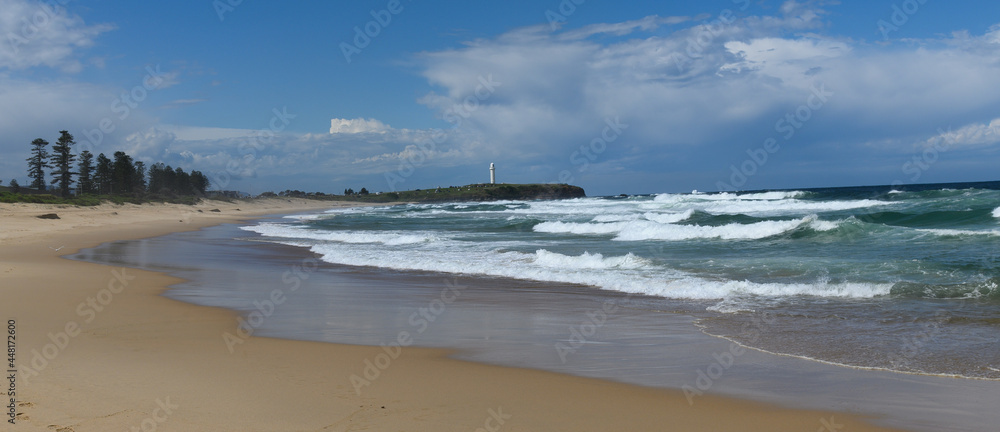 Beach view to a lighthouse with waves in the foreground