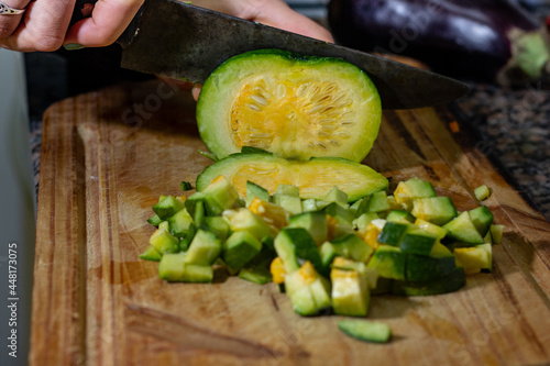 hands cutting an zucchini into slices on a wooden board with other vegetables. A fresh meal is being cooked © Ruben