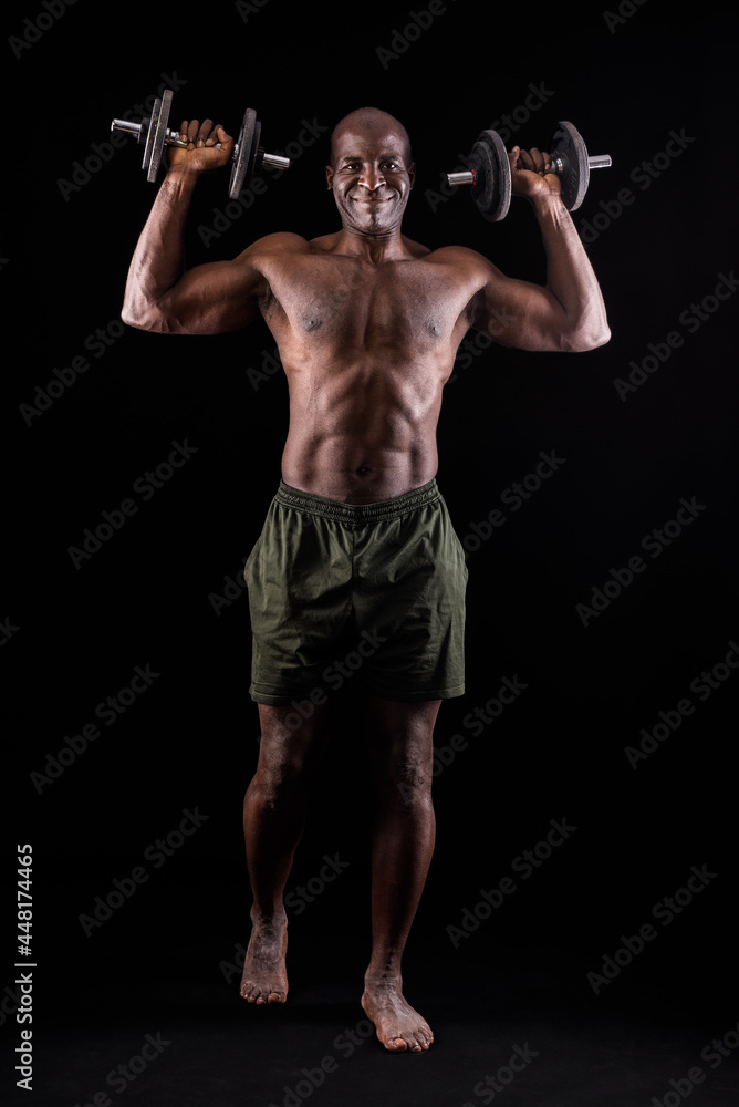 Athletic adult man doing shoulder exercise with dumbbells on a black background