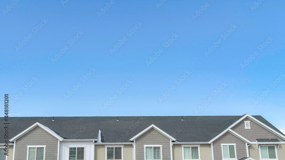 Pano Upper storey of suburban homes with gray roofs and dormers against blue sky Pano Upper storey of suburban homes with gray roofs and dormers against blue sky