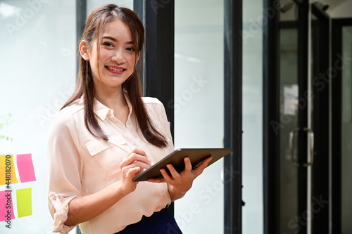 Cheerful Asian businesswoman holding digital tablet and smiling to camera.
