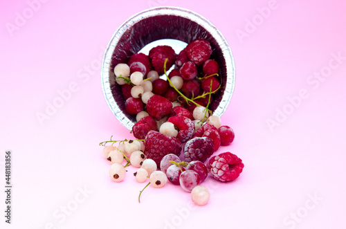 A set of frozen raspberries and currants of red and white color in a foil plate on a light background