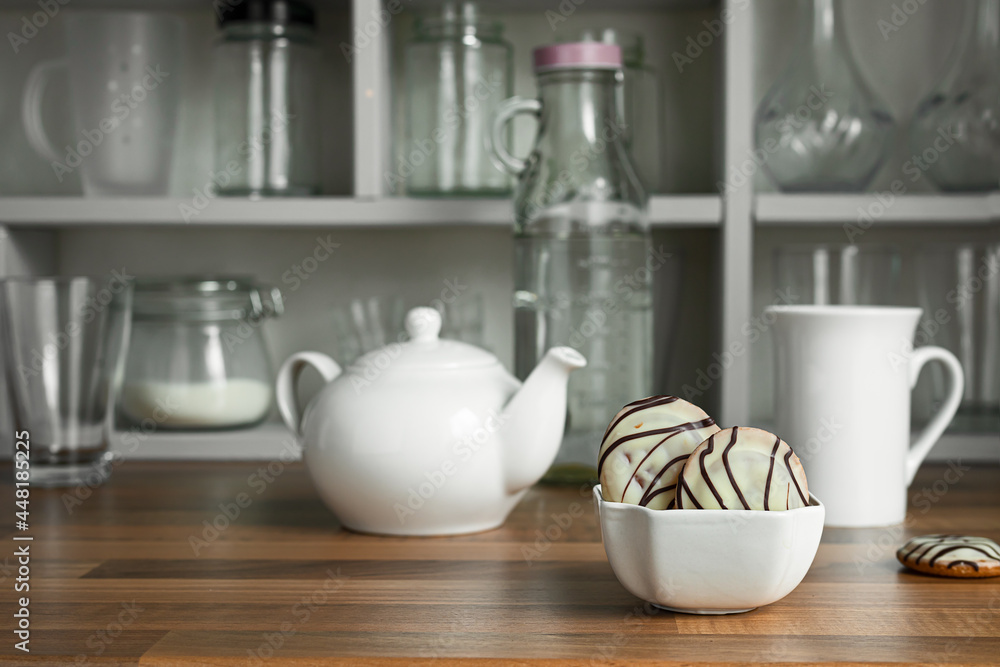 White teapot with tea cup and cookies in white bowl on the countertop of a Scandinavian-style kitchen, teatime and breakfast concept White teapot with tea cup and cookies in white bowl on the countertop of a Scandinavian-style kitchen, teatime and breakfast concept