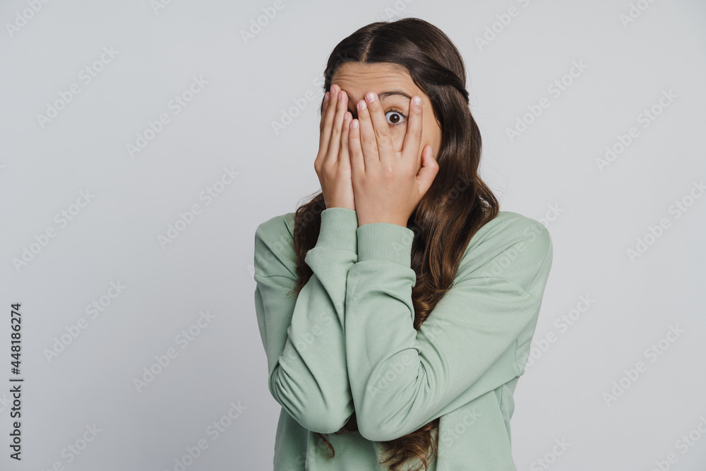 Beautiful girl closes her eyes with her hands, looking through her fingers. The girl spies with fear through her fingers Beautiful girl closes her eyes with her hands, looking through her fingers. The girl spies with fear through her fingers