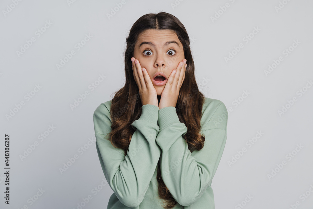Beautiful teenage girl touches her face with her hands, looks at the camera in shock. Girl isolated on a white background Beautiful teenage girl touches her face with her hands, looks at the camera in shock. Girl isolated on a white background