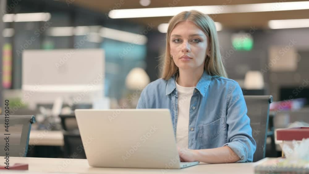 Woman Looking at Camera while using Laptop in Office Woman Looking at Camera while using Laptop in Office