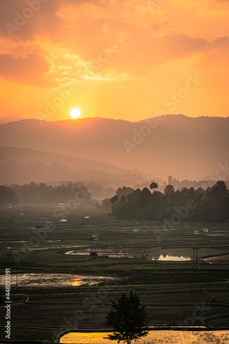 sunrise over mountains with country side farming fields and orange dramatic sky at dawn at village