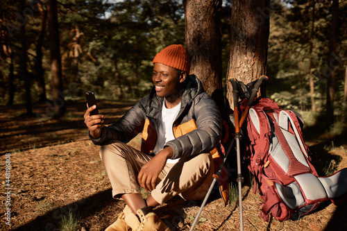 Happy black guy talking to family on video conference. Chilling on fresh air, weekend in forest for camping and hiking activity. Time for adventures, exploring, travelling, technology concept
