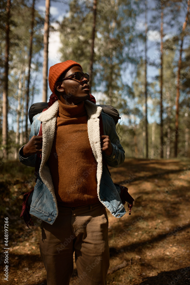 Well dressed afro american man wandering in forest and explore new places. Time away from civilization, wild nature. Sunset over trees, looking for camping place. Travelling, adventure time concept Well dressed afro american man wandering in forest and explore new places. Time away from civilization, wild nature. Sunset over trees, looking for camping place. Travelling, adventure time concept