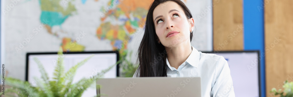 Naklejka premium Pensive young woman sits at laptop and looks up