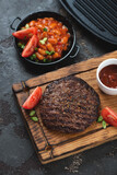 Wooden serving tray with grilled balkan meat patty or pljeskavica and prebranac, studio shot on a brown stone background, elevated view