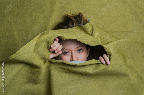 Young woman peeking out of green ripped fabric