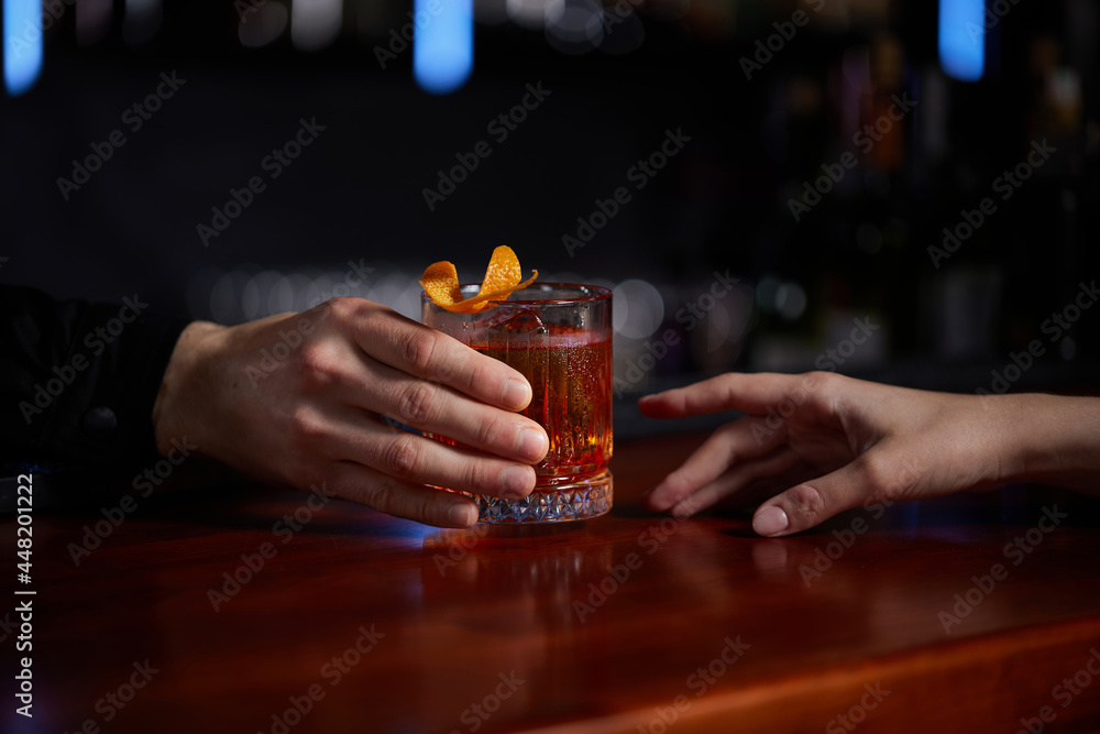 Barman holding out glass with alcoholic cocktail to the client