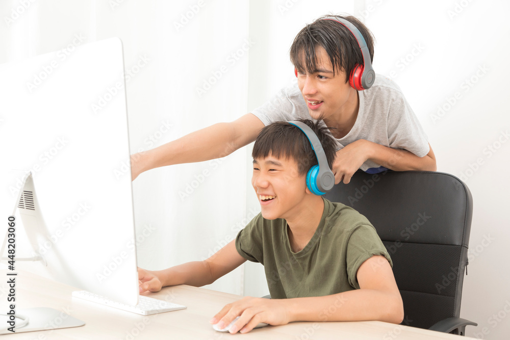 Obraz premium Two multiethnic teenage boys with headphone have fun with computer games at home.