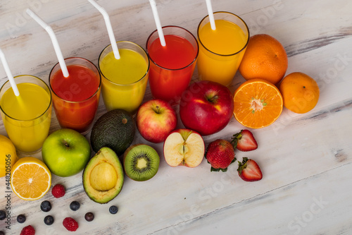 Different fruits juice in glass, apple, orange and strawberry juice with straw, looking refreshing on colourful wood board in front of white wall background. Picture decorating with fresh fruits