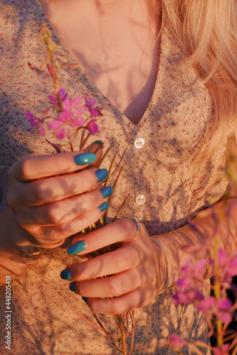 A young woman in a beautiful light dress holding pink flowers in her hands 