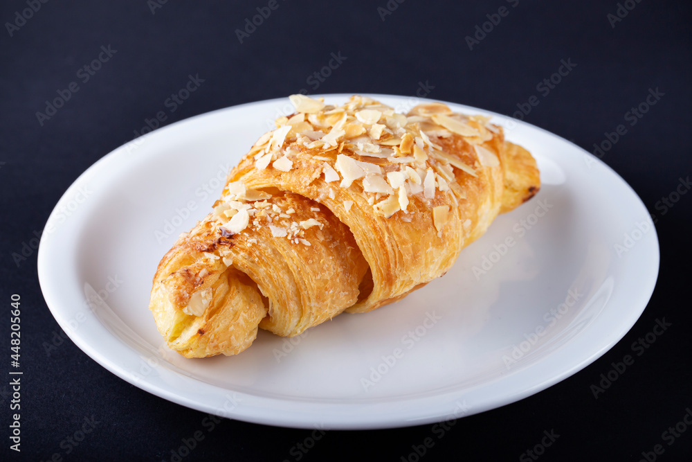 Fresh croissant with almonds on a white plate.