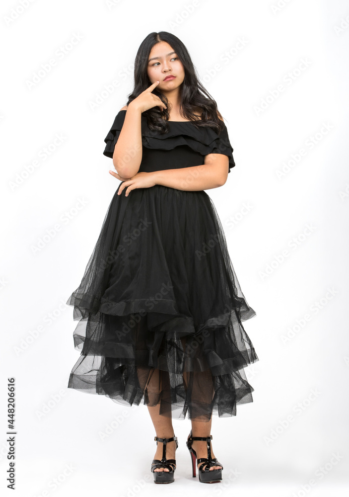 Full-body portrait shot a cute smiling young girl teenager in a beautiful black dress raising hand up and looking at camera in studio isolated white background. Junior girl dancing with happiness Full-body portrait shot a cute smiling young girl teenager in a beautiful black dress raising hand up and looking at camera in studio isolated white background. Junior girl dancing with happiness