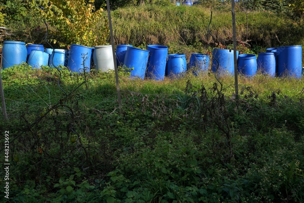 Plastic barrels for fermentation of fruits. They are arranged in row in garden in autumn. The barrels are in different shades of blue color. There is copy space in the foreground. Plastic barrels for fermentation of fruits. They are arranged in row in garden in autumn. The barrels are in different shades of blue color. There is copy space in the foreground.