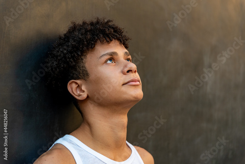 Afro latin male teenager against a wall, looking up.