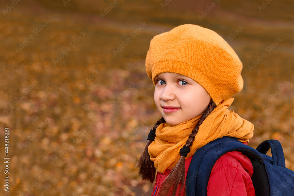 Little girl in a yellow beret on a background of autumn glade with fallen leaves. A child with a backpack goes to school Little girl in a yellow beret on a background of autumn glade with fallen leaves. A child with a backpack goes to school