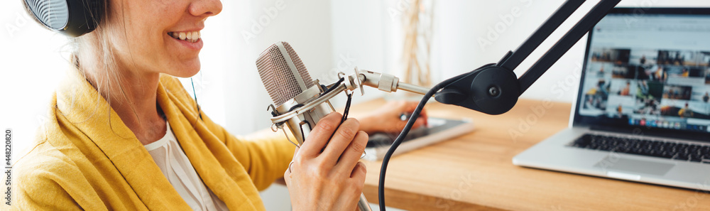 Wide image. Smiling female radio host recording and broadcasting her  podcast from homemade studio. Woman talk into microphone on table foto de  Stock | Adobe Stock
