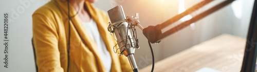 Woman radio host recording and broadcasting her podcast from homemade studio. Female podcaster talk into microphone on table. Wide image. Close-up