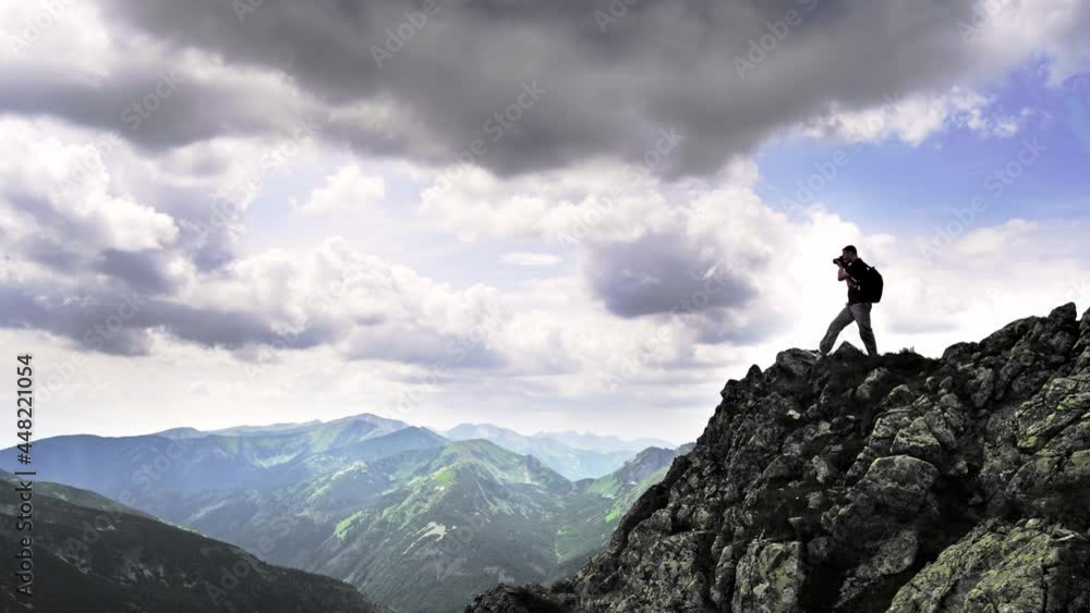 Back view of a tourist, standing on the edge of a high mountain and take a photo of the beautiful landscape on a sunny summer day Back view of a tourist, standing on the edge of a high mountain and take a photo of the beautiful landscape on a sunny summer day