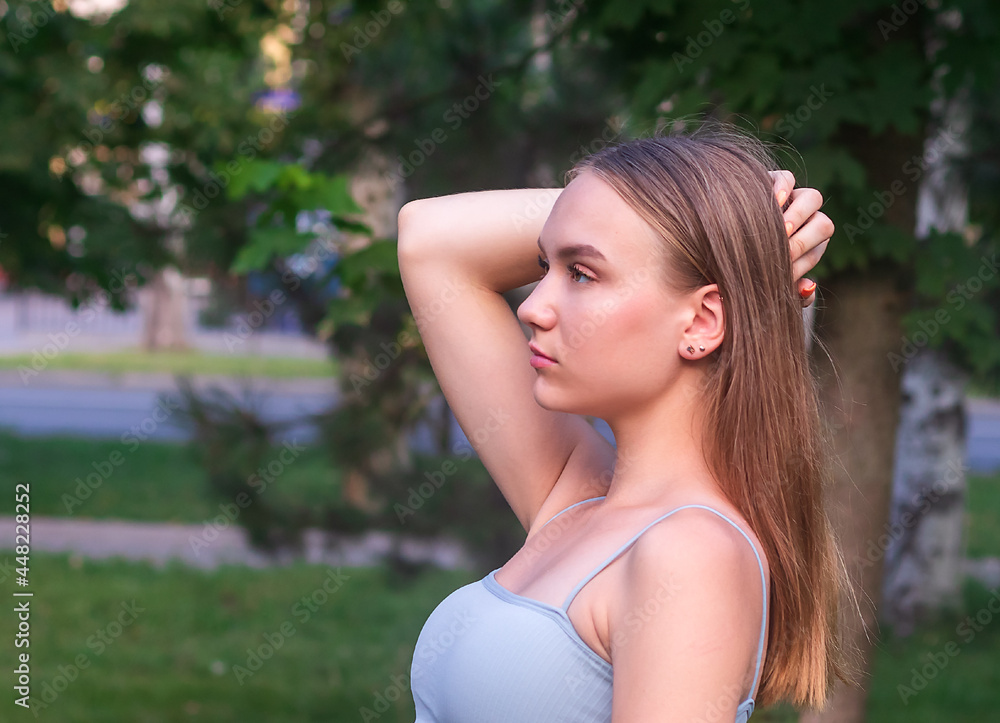 Naklejka premium portrait in profile of a young beautiful girl 16 years old, with long hair, against a background of green nature