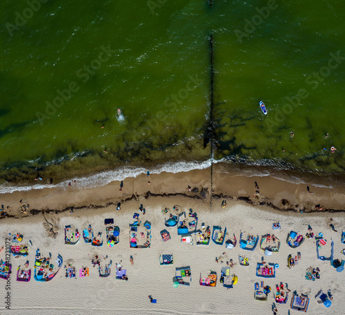 Morze i piaszczysta plaża z opalającymi i kąpiącymi się plażowiczami w miejscowości Sarbinowo, widok z lotu ptaka