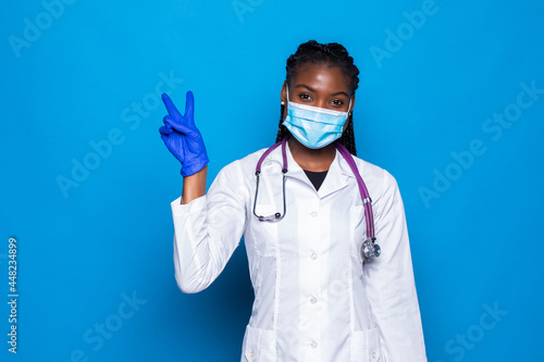 Pretty african american doctor woman isolated on blue background in studio in white medical gown showing victory sign. Healthcare personnel health medicine concept.