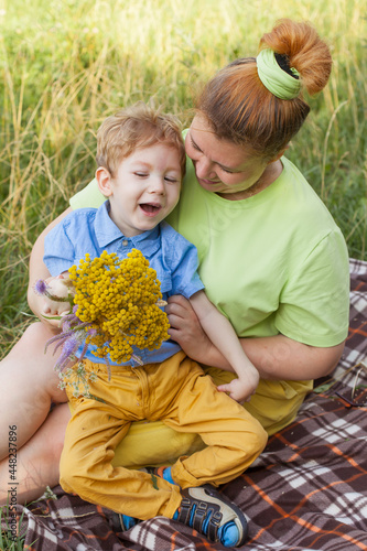A happy mother and a disabled child are sitting on the grass in the park and gently hugging. Summer holidays. Disability.